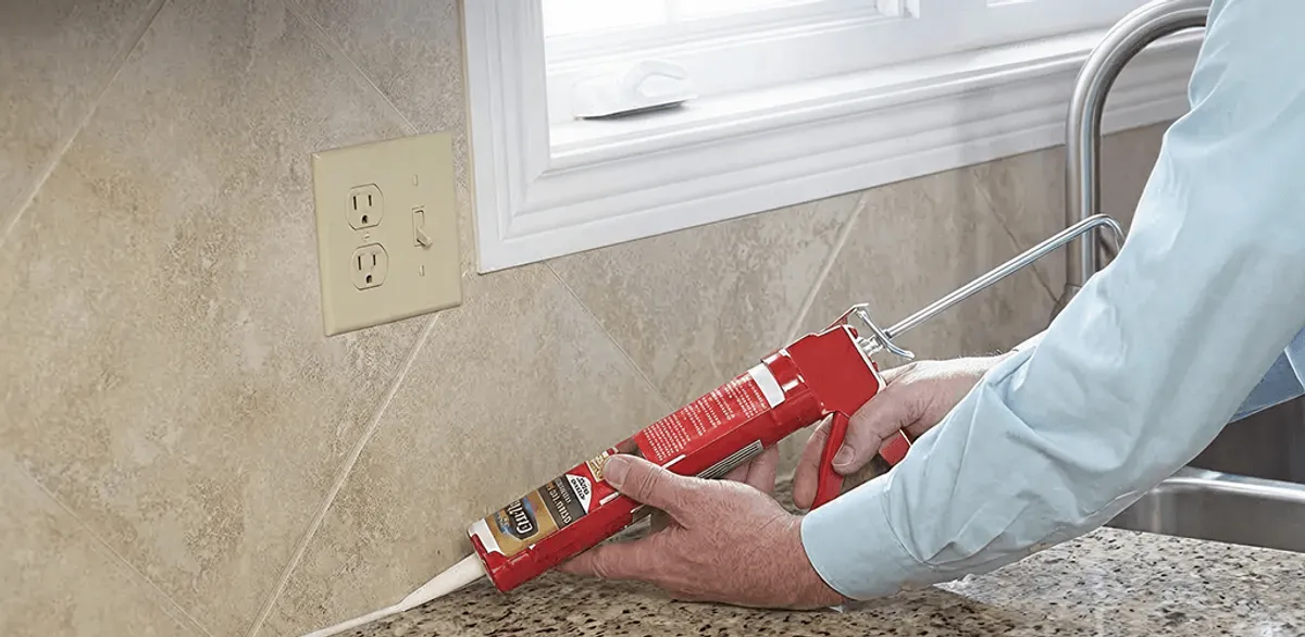 Handyman applying caulk along a kitchen backsplash and countertop seam in Bloomington, IN