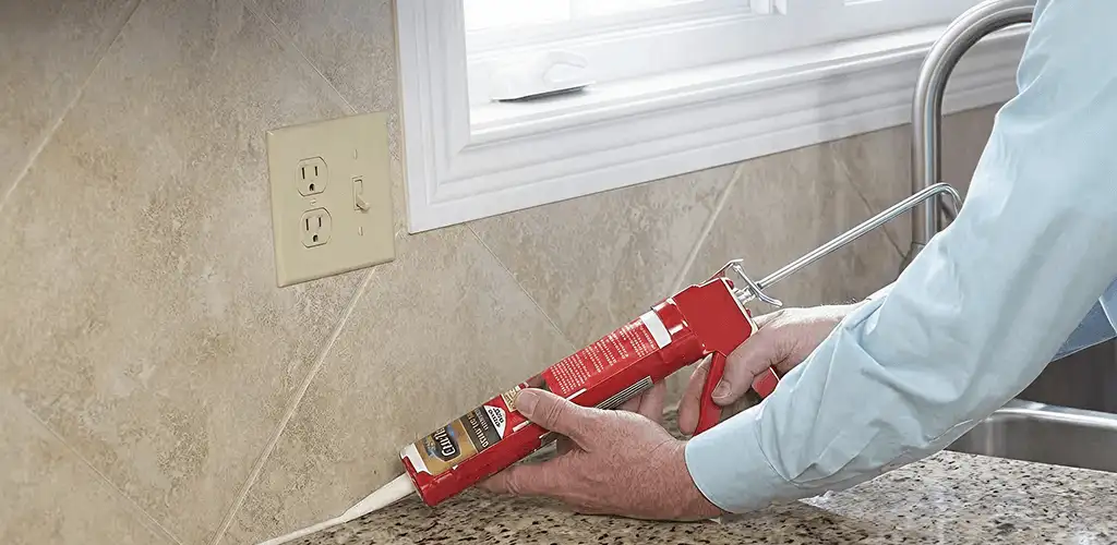 Handyman applying caulk along a kitchen backsplash and countertop seam in Bloomington, IN